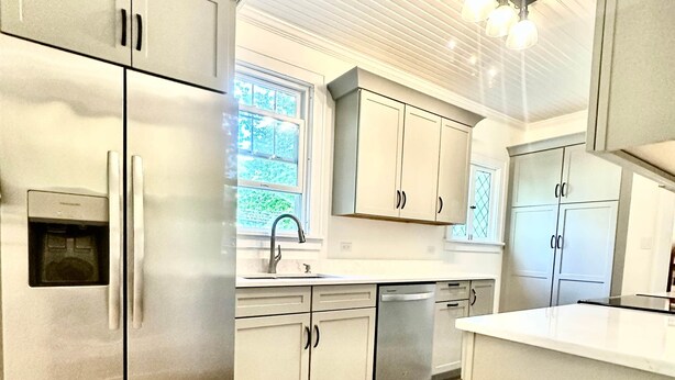 A modern kitchen with stainless steel appliances, light-colored cabinetry, and a large window providing natural light.