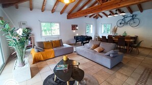 Een ruime woonkamer met een hoge plafond, houten balken, een bank, een salontafel en een eethoek met stoelen en een tafel.