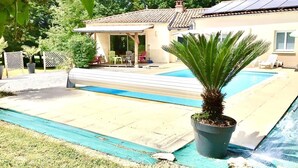 Een huis met een zwembad, een overdekt terras en een tuin.