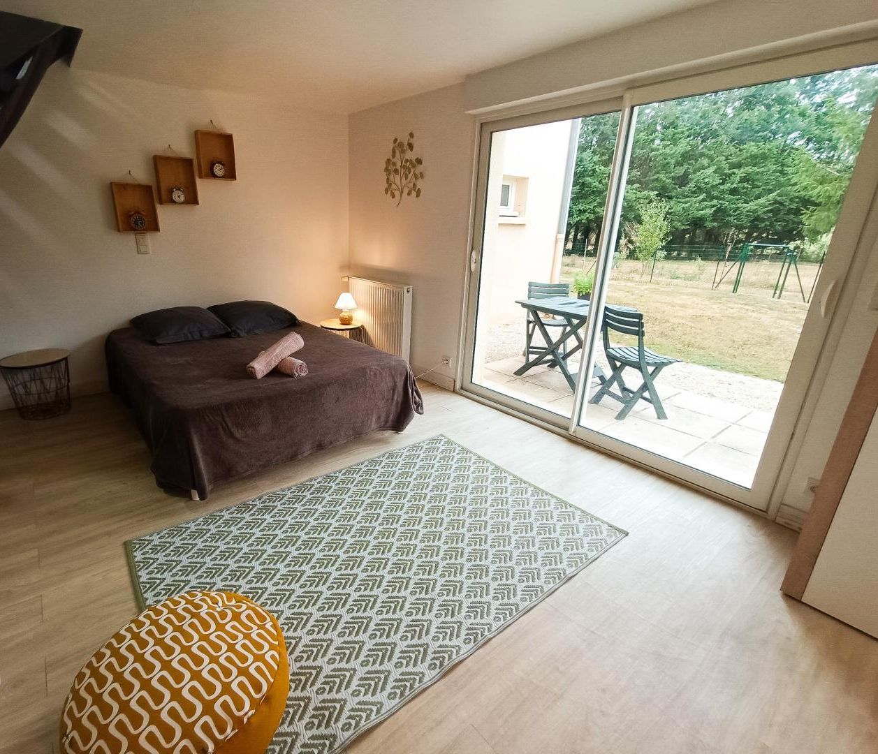 Une chambre avec un lit, une petite table avec une lampe, un tapis à motifs et une vue sur un patio extérieur avec des chaises et une table.