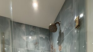 Una dutxera amb accés directe, porta de vidre, rajoles de marbre i mànega de dutxa.