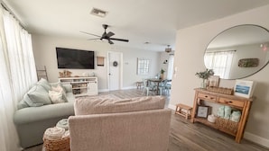 A living room with a sofa, a coffee table, a TV, a ceiling fan, and a dining area with a table and chairs. - Coastal Getaway • 2bd-2ba • 5 miles to boat ramp and Earl’s hideaway! (Sebastian)