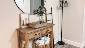 A wooden console table with a mirror, a framed picture, and wicker baskets. - Coastal Getaway • 2bd-2ba • 5 miles to boat ramp and Earl’s hideaway! (Sebastian)