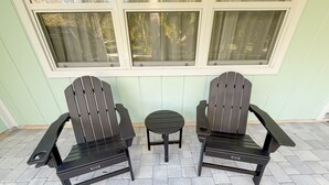 Two Adirondack chairs and a small round table on a paved patio with a window above. - Coastal Getaway • 2bd-2ba • 5 miles to boat ramp and Earl’s hideaway! (Sebastian)