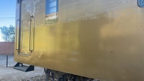 A yellow train car with visible wear and tear, a door, and a window. - Onkel Inn Wagon Sleepbox (Uyuni)