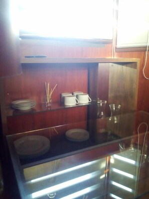 A kitchen with wooden cabinets, a glass shelf, and various kitchenware including plates, cups, and glasses. - Onkel Inn Wagon Sleepbox (Uyuni)