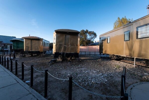 Vagones de tren antiguos estacionados sobre grava, rodeados por una cerca de alambre.