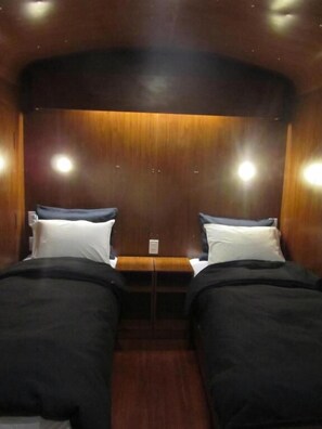 A room with two beds, wooden paneling, and ceiling lights. - Onkel Inn Wagon Sleepbox (Uyuni)