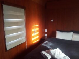 A hotel room with a bed, a wall-mounted heater, and a window with blinds.