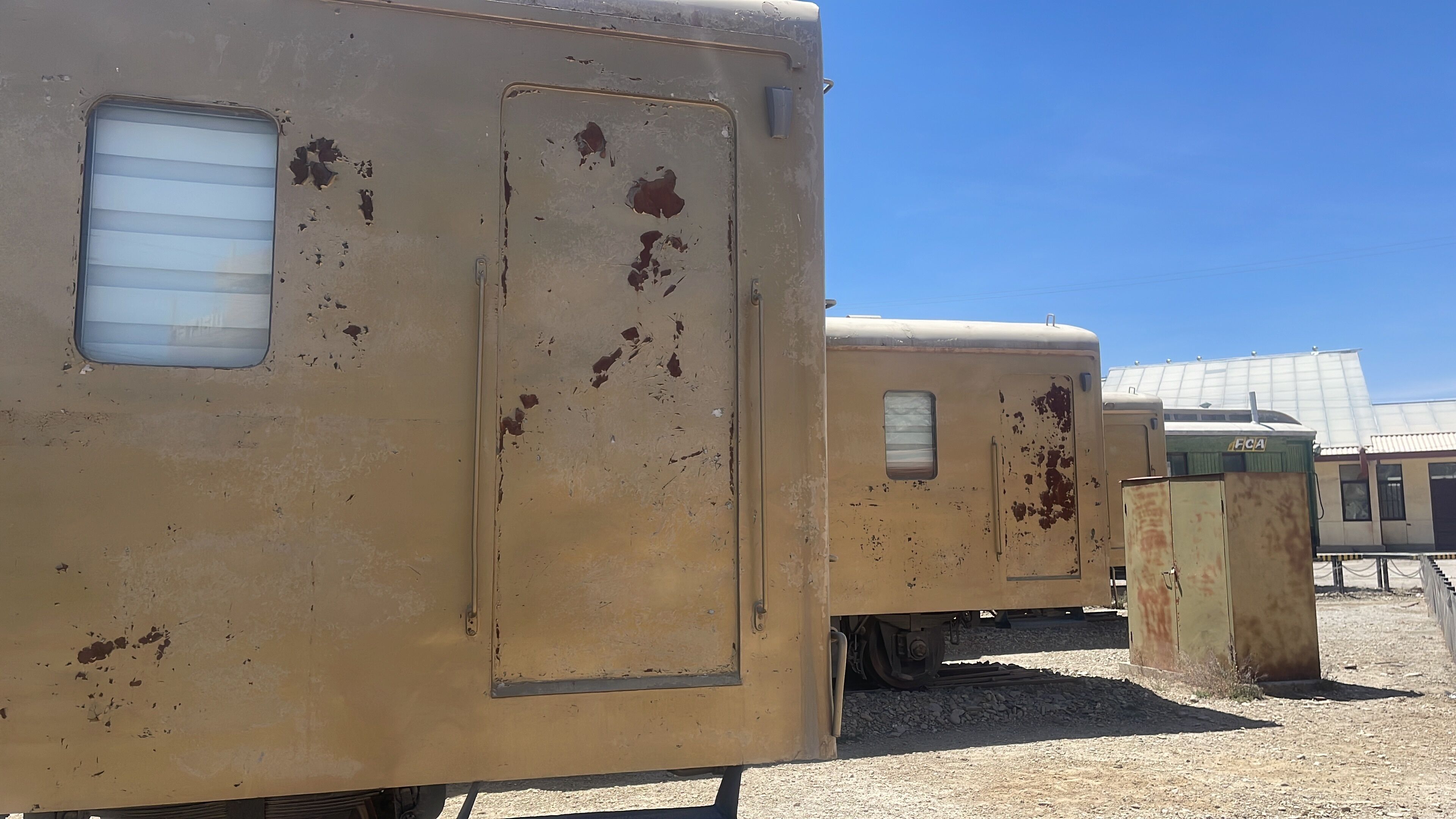 Un vagón de tren oxidado con una ventana y una puerta, parte de un conjunto ferroviario más grande.