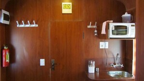 A compact kitchen with a microwave, sink, and a fire extinguisher. - Onkel Inn Wagon Sleepbox (Uyuni)