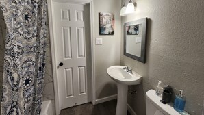 A bathroom with a white door, a sink, a toilet, and a shower curtain. - Luxury Apartment Unit 8 (El Paso)
