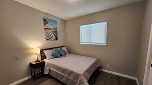 A bedroom with a bed, a nightstand, a lamp, a painting, and a window with blinds. - Luxury Apartment Unit 8 (El Paso)