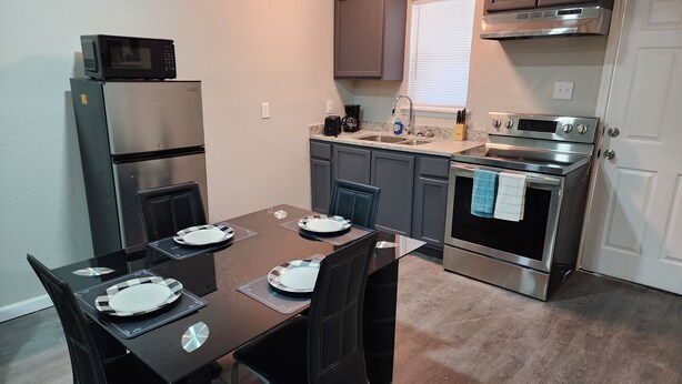 A compact kitchen with a dining table set for two, a refrigerator, microwave, oven, and a coffee maker. - Luxury Apartment Unit 8 (El Paso)