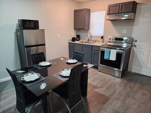 A compact kitchen with a dining table set for two, a refrigerator, microwave, oven, and a coffee maker. - Luxury Apartment Unit 8 (El Paso)