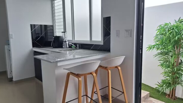 A modern kitchen with a marble countertop, two white bar stools, a black coffee machine, and a large window. - apto-wifi6-tvstreaming (Panamá)