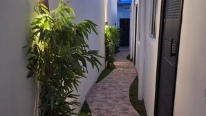 A narrow stone-paved corridor with white walls, green plants, and a blue-lit window at the end. - apto-wifi6-tvstreaming (Panamá)