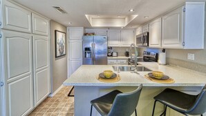 A modern kitchen with white cabinetry, a central island with bar stools, a stainless steel refrigerator, and a microwave. - Chic 1-bedroom, 2 baths condo in the heart of Palm Springs. (Palm Springs)