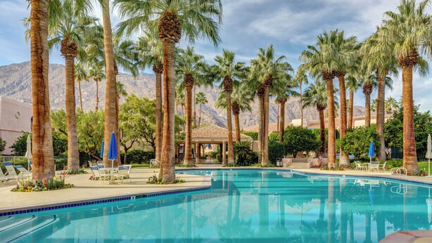 A pool area with palm trees, lounge chairs, and a covered seating area. - Chic 1-bedroom, 2 baths condo in the heart of Palm Springs. (Palm Springs)