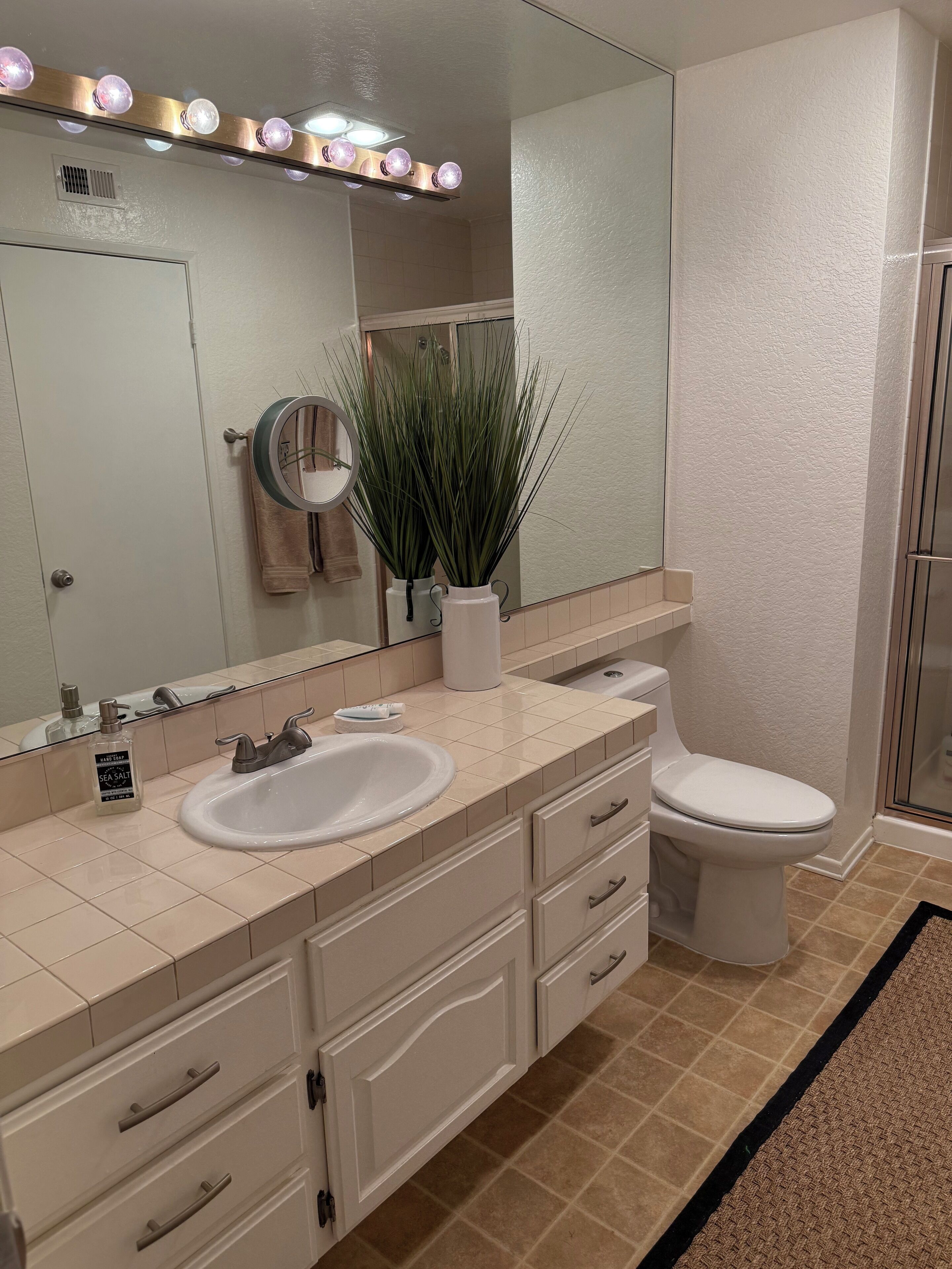 A bathroom with a double sink, a toilet, a mirror, and a shower.