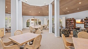 A spacious indoor area with a high ceiling, wooden beams, and a skylight. There are multiple seating areas with wicker furniture and a large bookshelf filled with books. - Chic 1-bedroom, 2 baths condo in the heart of Palm Springs. (Palm Springs)