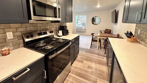 Une cuisine moderne avec des meubles de couleur sombre, une cuisinière en acier inoxydable et un four à micro-ondes. On y trouve un coin repas avec une table et des chaises, ainsi qu’une fenêtre qui laisse entrer la lumière naturelle.