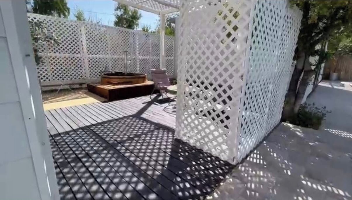 A covered outdoor patio with a wooden deck, a built-in seating area, and a white lattice fence.