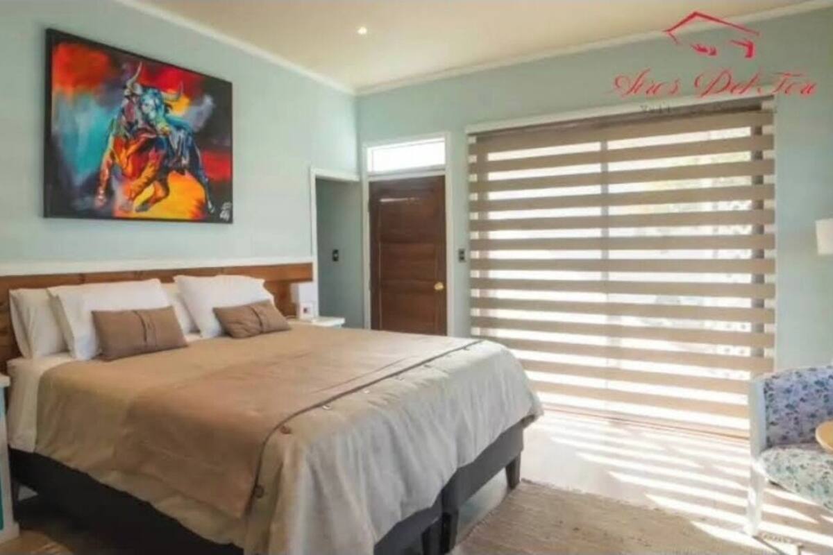 Quarto com cama, mesas de cabeceira, um quadro e janela com persianas.