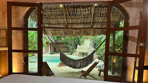 A room with a large bed, a hammock, and a view of a swimming pool and lush greenery. - Casa Yaxunah II 30 min from Chichen (Yaxuna)