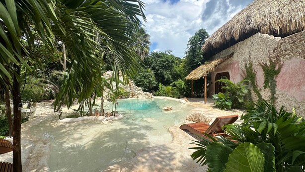 A tropical pool area with a thatched-roof structure, surrounded by lush greenery and a clear pool. - Casa Yaxunah II 30 min from Chichen (Yaxuna)
