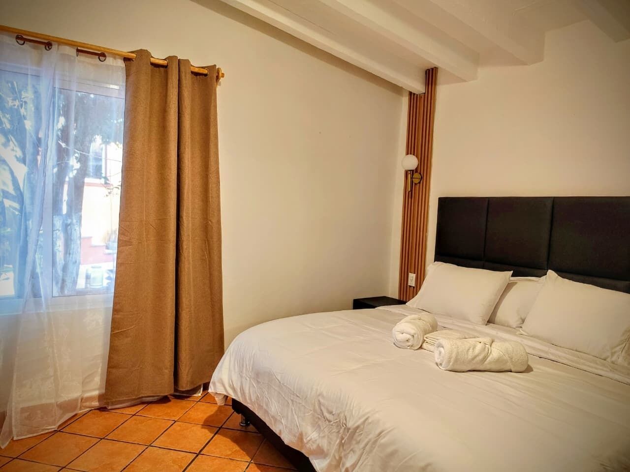 A hotel room with a bed, a nightstand, a lamp, and a window with curtains.