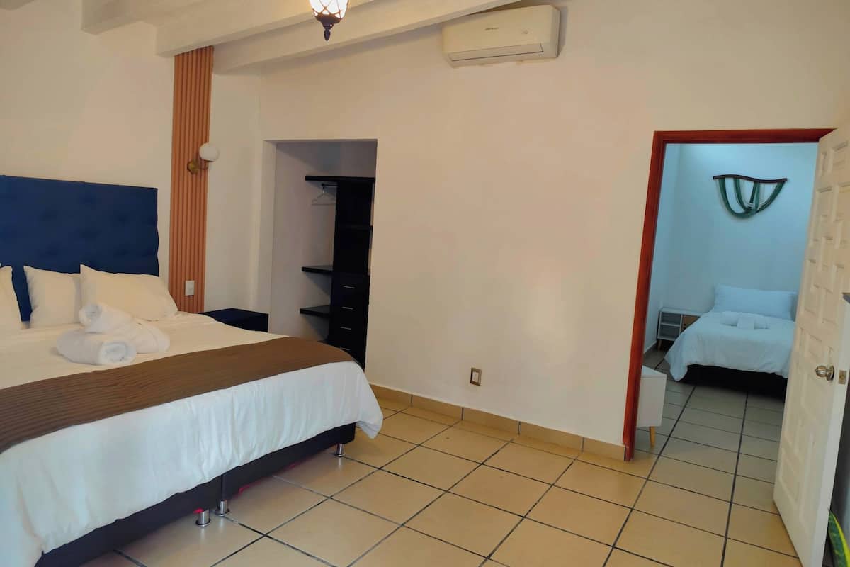 A hotel room with a bed, a wardrobe, a hanging light fixture, and an air conditioning unit.