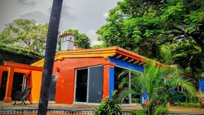 A colorful building with a large open door, surrounded by lush greenery and a palm tree. - Hotel Eterna Primavera Cuernavaca (Cuernavaca)
