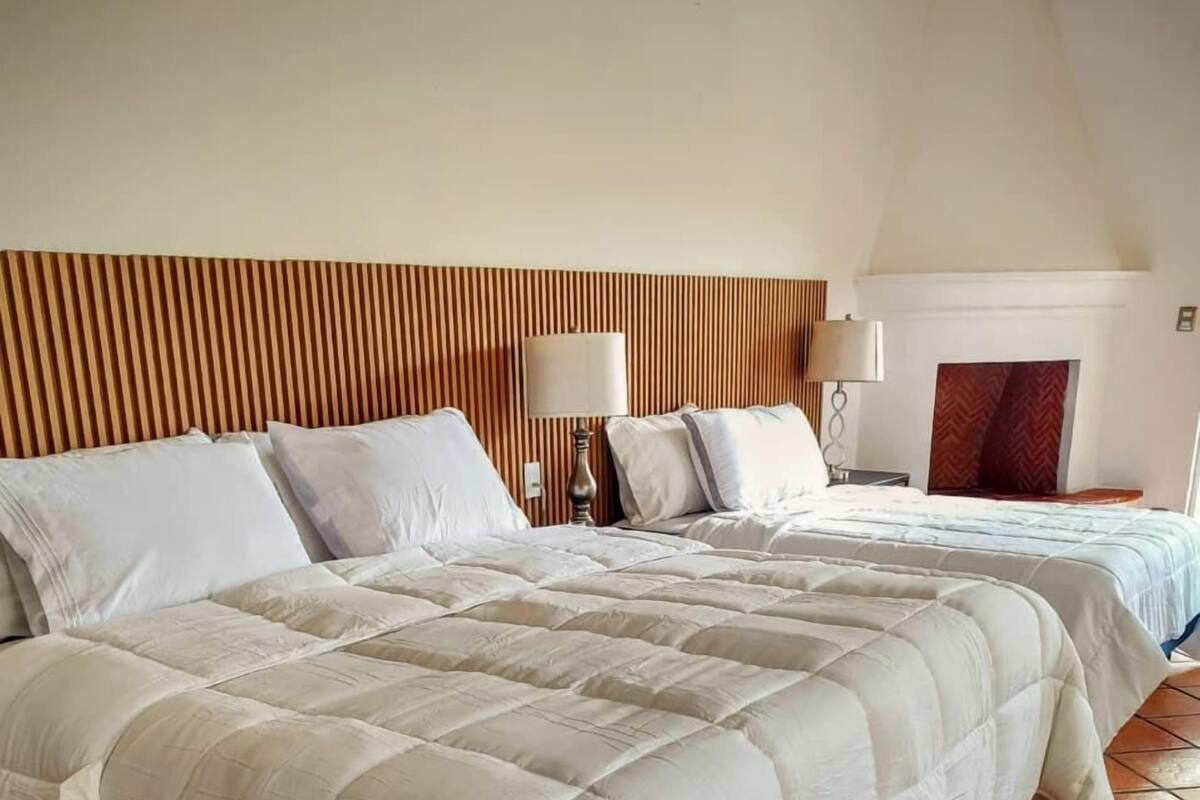 A hotel room with two beds, a wooden headboard, a tiled floor, and a nightstand with a lamp.