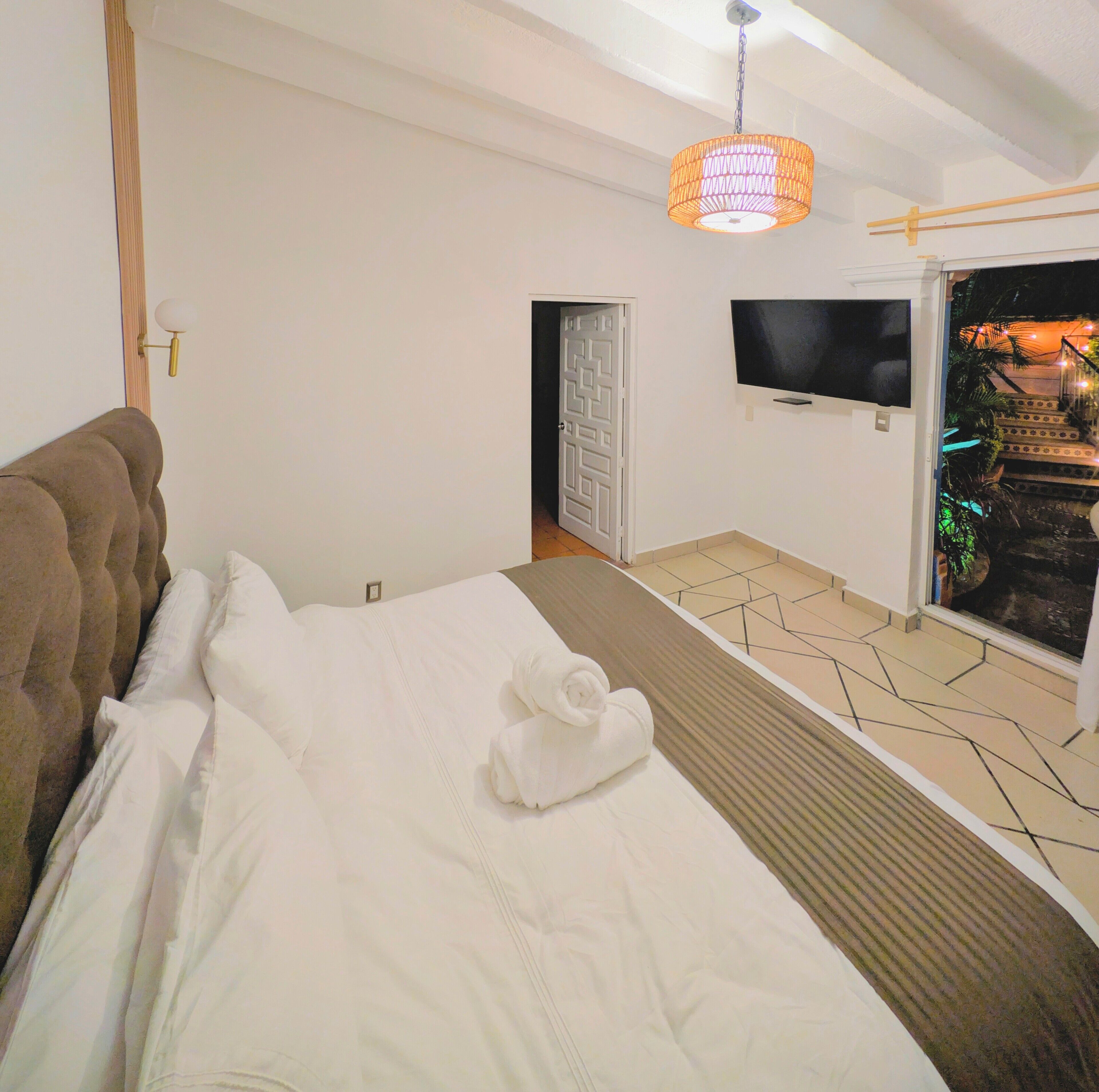 A bedroom with a bed, a TV mounted on the wall, and a door leading to an outdoor area with plants.
