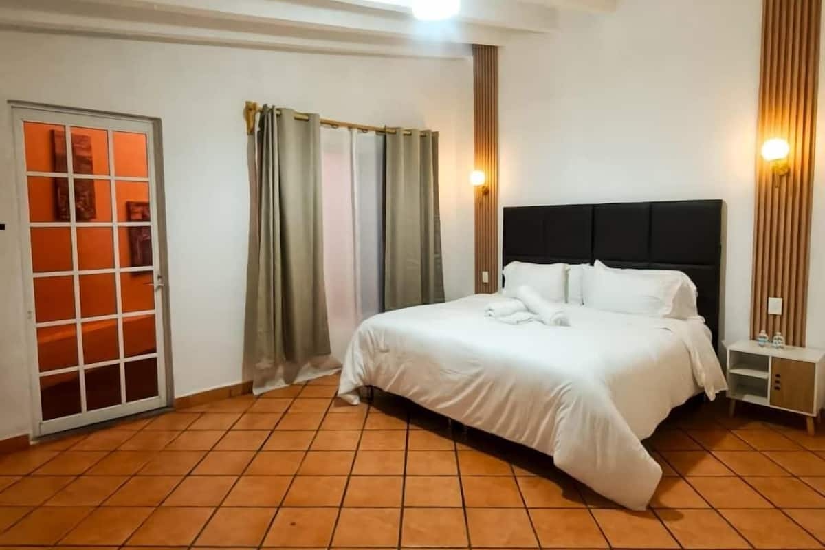 A bedroom with a bed, a nightstand, a wall-mounted light, and a sliding door.