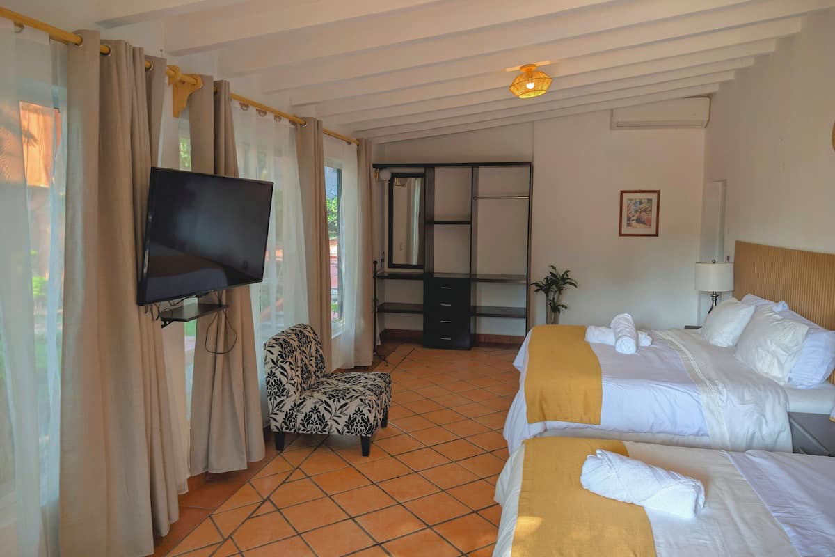 A hotel room with two beds, a TV, a chair, a desk, and a large window with curtains.