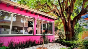 A pink building with large windows, surrounded by greenery and a large tree. - Hotel Eterna Primavera Cuernavaca (Cuernavaca)