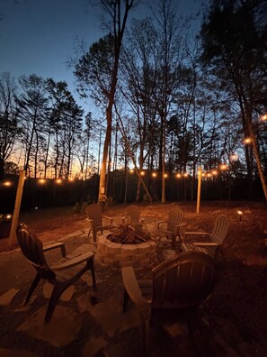 An outdoor seating area with Adirondack chairs and a fire pit, surrounded by trees and string lights. - Cozy Family-Friendly Cabin with Deer Sightings (Blairsville)