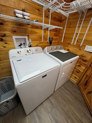 A laundry room with two Maytag washers and dryers, wooden walls, and a metal shelf above the dryers.