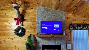 Una habitación acogedora con chimenea de piedra, paredes de madera, un televisor en un estante de piedra y un adorno circular en la pared.