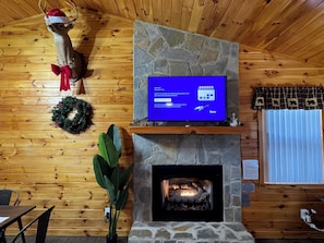 A cozy room with a stone fireplace, wooden walls, a television on a stone shelf, and a wreath on the wall. - Cozy Family-Friendly Cabin with Deer Sightings (Blairsville)
