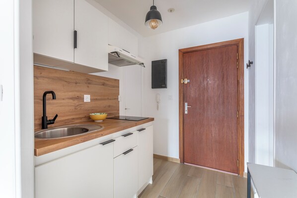Una cocina moderna con armarios blancos, encimera de madera, grifo negro y puerta de madera.
