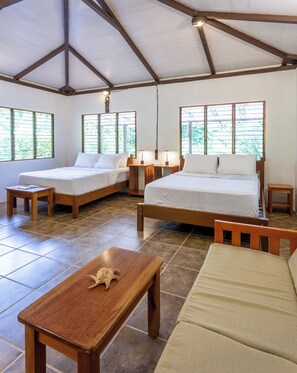 Una habitación con dos camas, una mesa de madera, un sofá y ventanas amplias con vistas a zonas verdes.