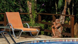 Zona de piscina con una silla de descanso, una estatua y una valla de madera.