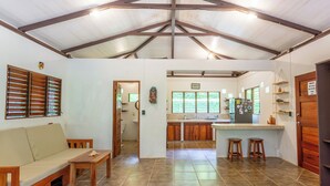 Amplia sala de estar con techo alto, cocina con muebles de madera y comedor con taburetes.