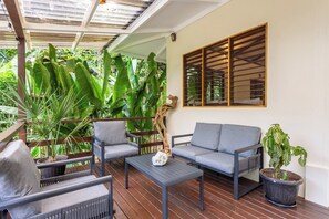 A covered outdoor seating area with a sofa, chairs, and a coffee table, surrounded by large green plants and a wooden trellis. - Best Location Cabo Matapalo Jungle Surfside Cabin (Puerto Jimenez)