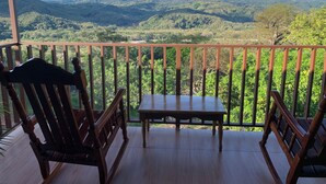 Een houten terras met twee stoelen en een tafel, met uitzicht op een bergachtig landschap.