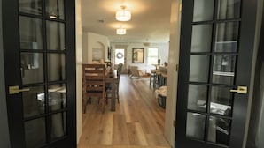 Un couloir avec un plancher en bois, un coin repas avec une table et des chaises, et un espace cuisine avec un évier et un comptoir.
