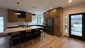 A modern kitchen with a central island, bar stools, and a large refrigerator.